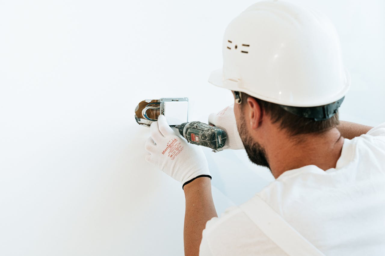 Services Construction worker wearing helmet and gloves uses a power tool to fix a wall.